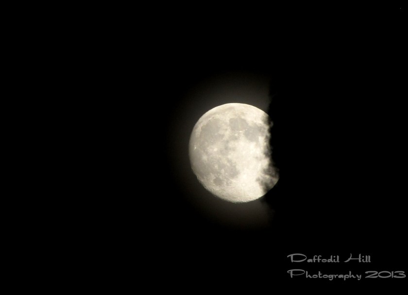 A hand held shot of the moon being eating by a cloud.